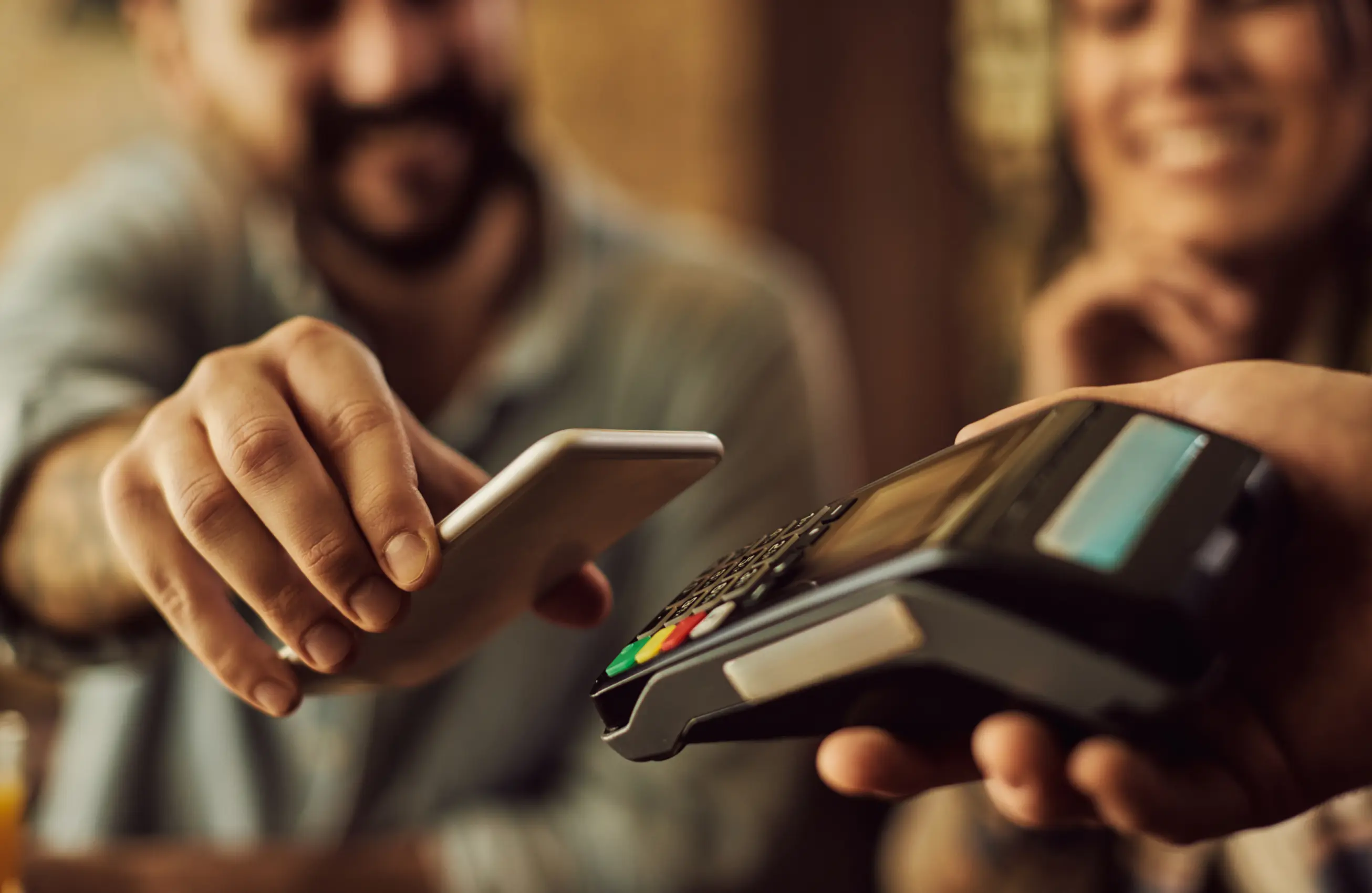 Um homem segurando um celular próximo de uma máquina de cartão que outra pessoa está segurando. 