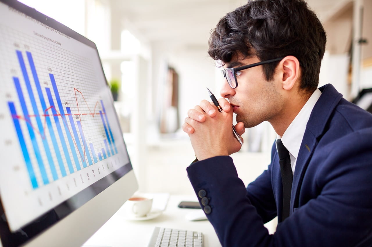 Pessoa analisando gráficos de desempenho financeiro em uma tela de computador, com expressão de concentração e foco na análise de dados.