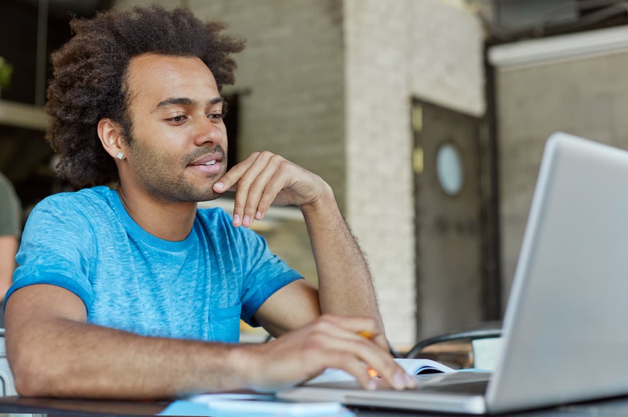 Homem com cabelo afro e camiseta azul olhando pensativo para a tela de um notebook. Ele está pesquisando se a cobrança de CET é legal.