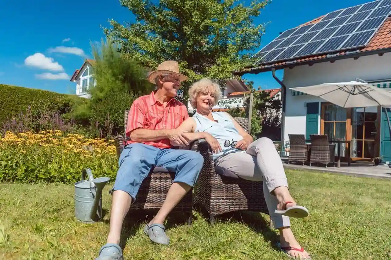 Casal de idosos relaxando em jardim ensolarado, desfrutando dos benefícios do financiamento para energia solar.