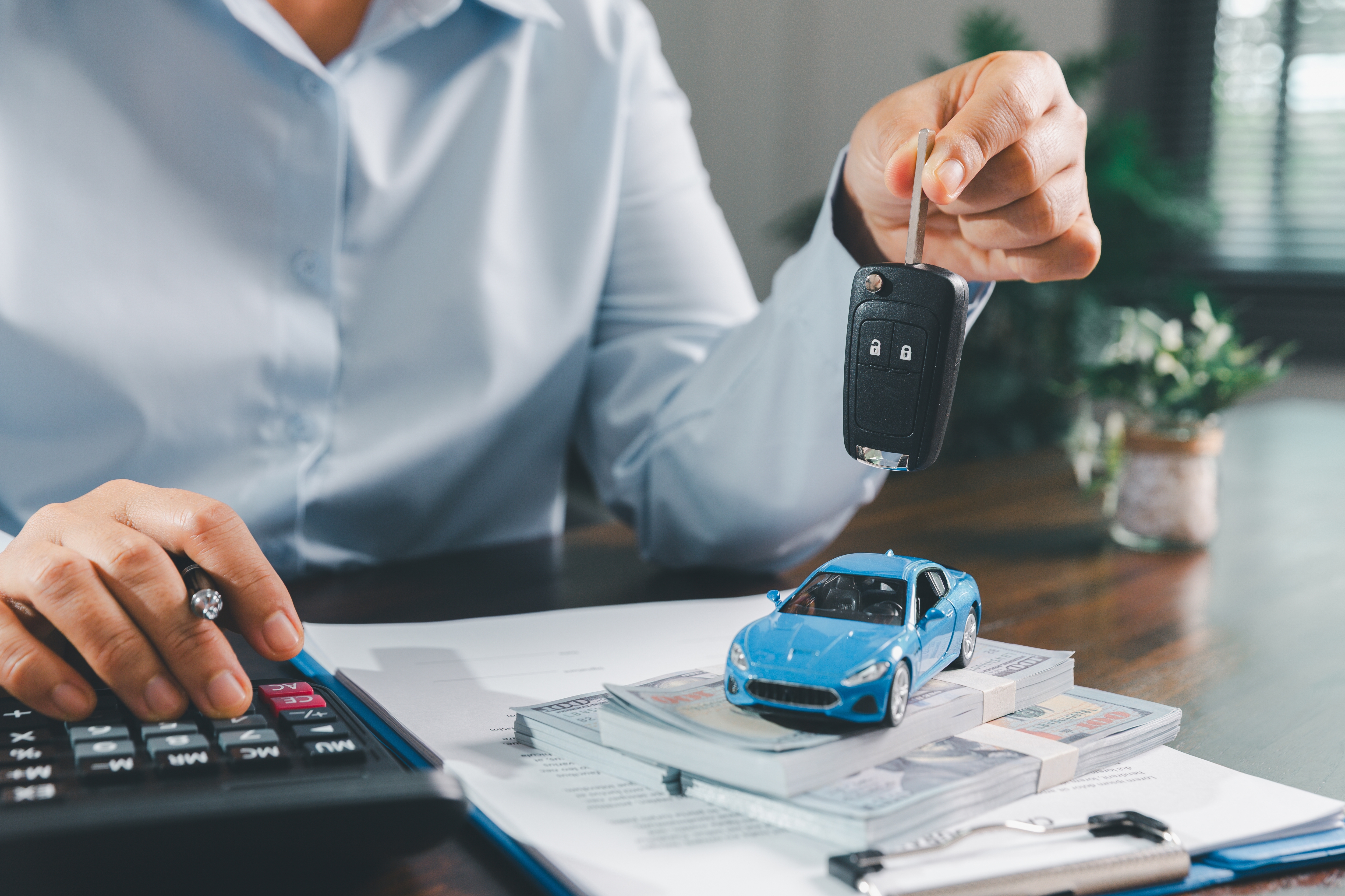 homem com calculadora em uma mão e chave de um carro na outra