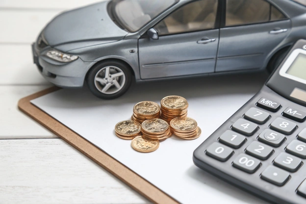 Modelo em miniatura de carro cinza sobre uma prancheta com pilhas de moedas douradas ao lado de uma calculadora, simbolizando IBV Auto.