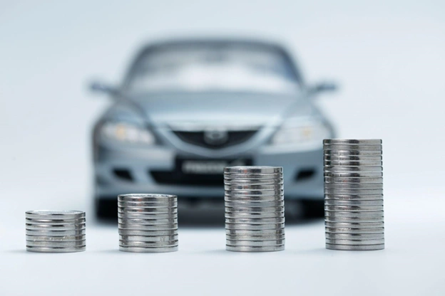 miniatura de carro prateado ao fundo com quatro pilhas de moedas em ordem crescente à frente, representando a valorização e o aumento no valor do veículo medido pelo IBV Auto.