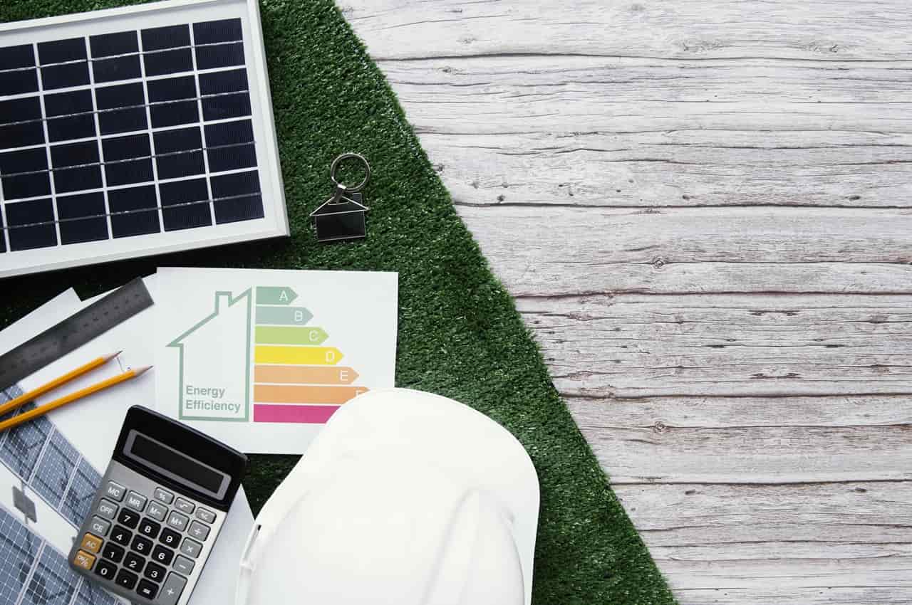 Vista superior de uma superfície dividida entre madeira e grama sintética, contendo um pequeno painel solar, capacete branco, calculadora e um gráfico de eficiência energética.