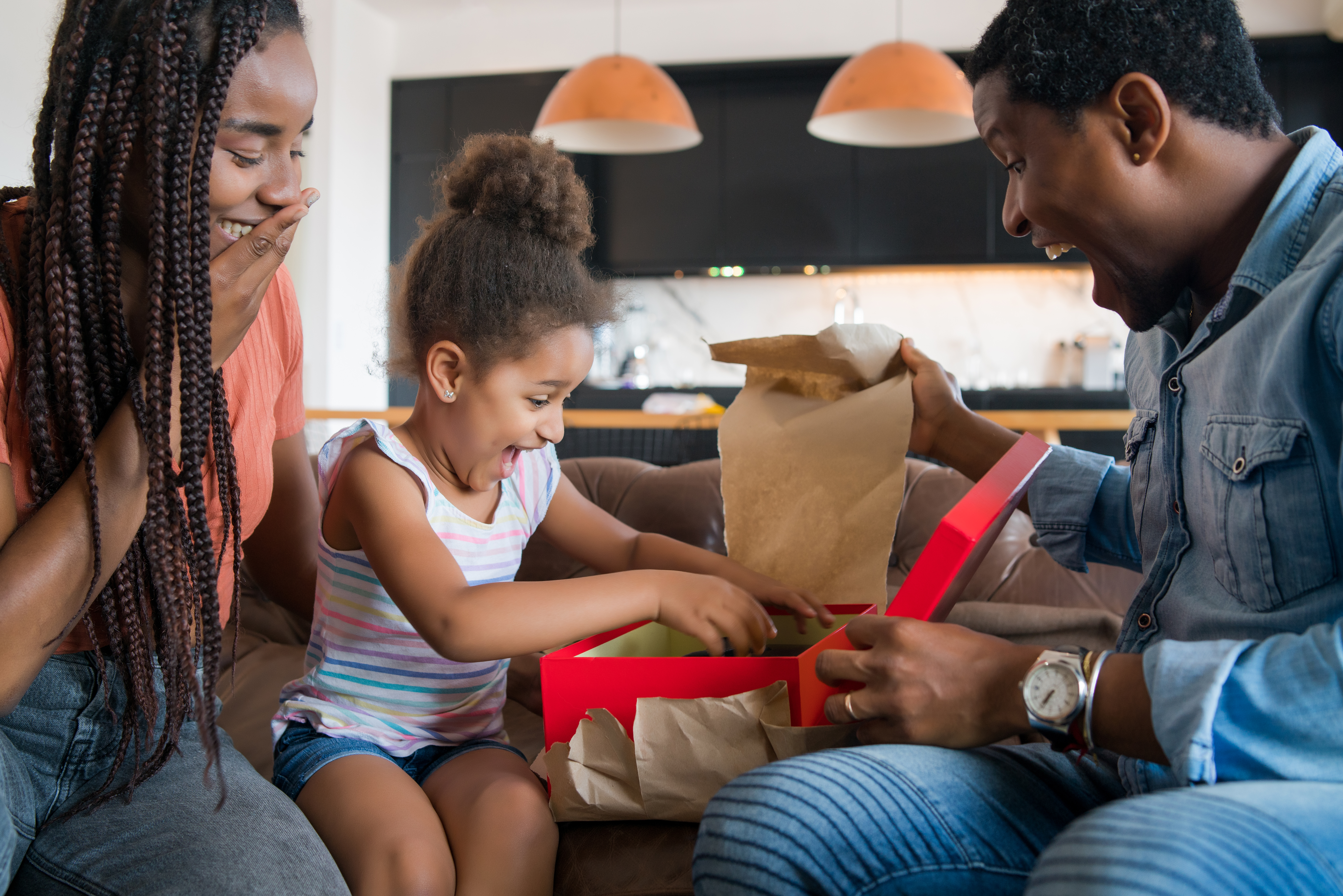 criança abrindo caixa de presente junto dos pais