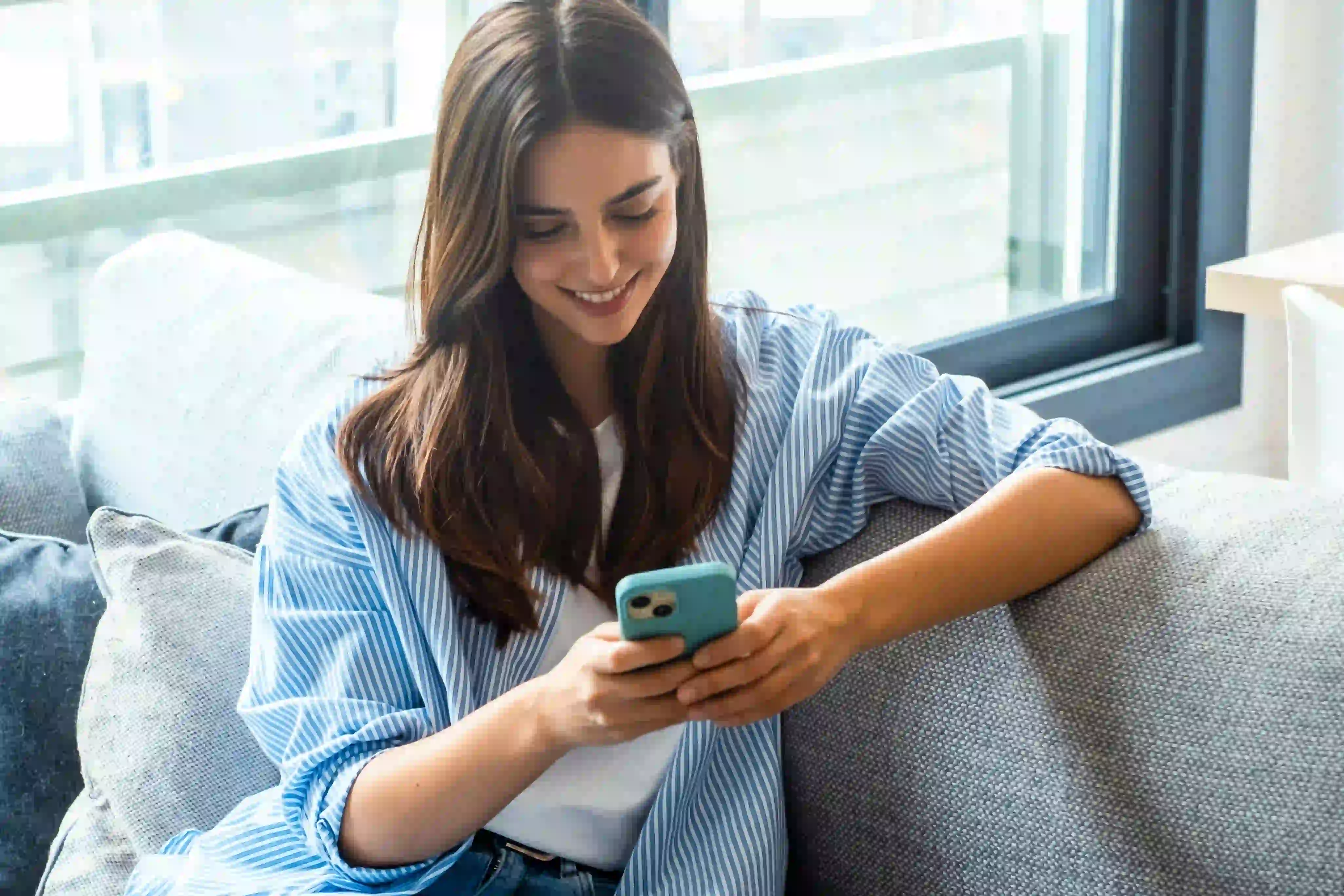 mulher feliz sentada no sofá mexendo no celular