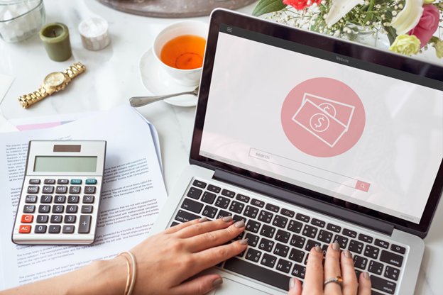 pessoa usando notebook com ícone de dinheiro, calculadora e documentos sobre a mesa.