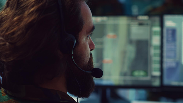 Homem com headset olhando para monitores de computador.