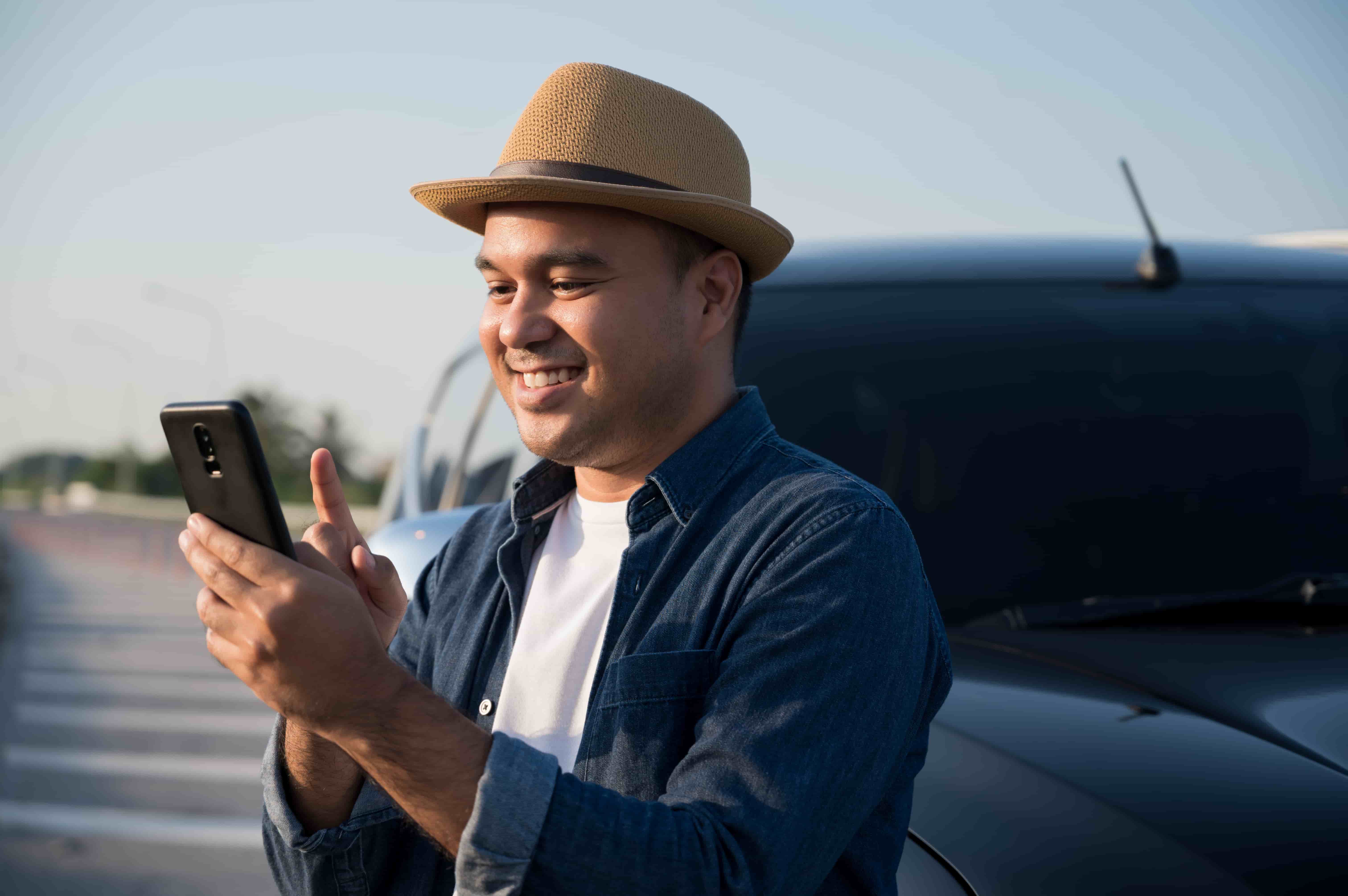 Homem em frente a um carro estacionado, com o celular na mão