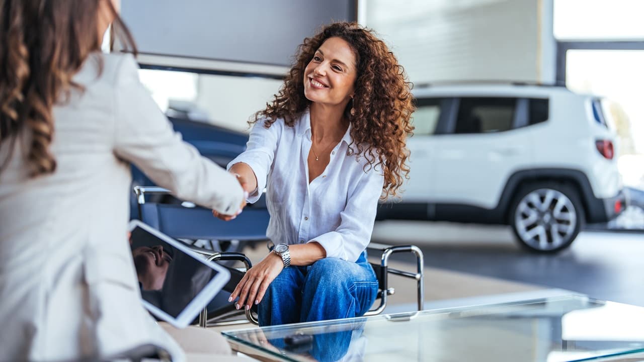 mulher em concessionária de carros, sorrindo e apertando a mão de vendedora.
