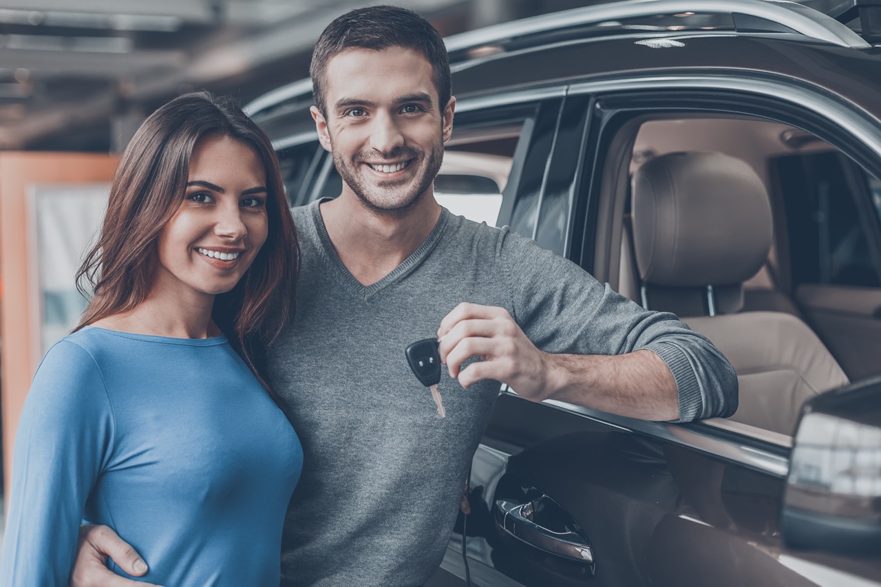 Mulher e homem ao lado de um carro preto, homem segurando a chave.