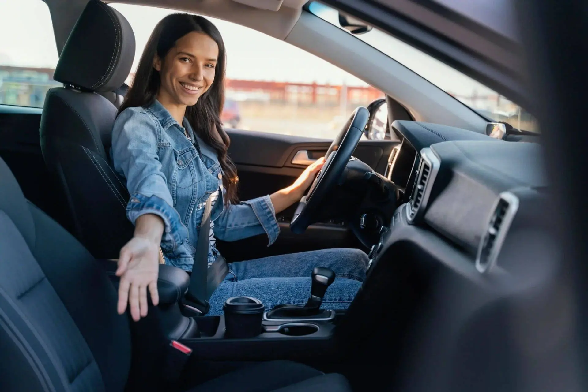 A imagem mostra uma mulher dirigindo seu carro. Ela está sorridente.