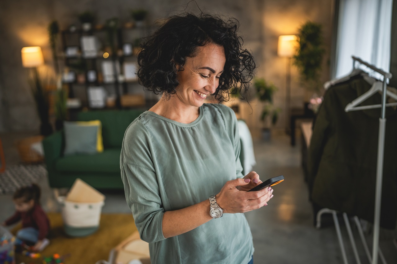 Mulher em pé, sorrindo com celular na mão
