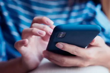 Uma pessoa segurando um smartphone com uma capa protetora azul-escura. A pessoa usa uma camisa listrada em azul e branco.