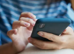 Uma pessoa segurando um smartphone com uma capa protetora azul-escura. A pessoa usa uma camisa listrada em azul e branco.