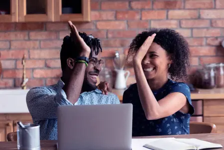 Duas pessoas comemorando com um cumprimento animado em frente a uma tela de notebook.