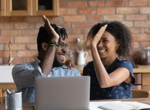 Duas pessoas comemorando com um cumprimento animado em frente a uma tela de notebook.