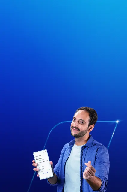Imagem com fundo azul, com um homem branco, sorrindo. Na mão direita, ele faz um sinal e na esquerda segura um celular.