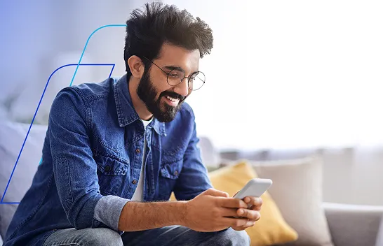 Homem sorridente de óculos, usando o celular sentado no sofá