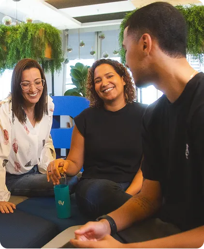 Time de profissionais, sendo 2 mulheres e 1 homem, conversando no escritório do banco BV