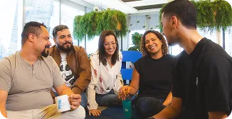 Time de profissionais, sendo 2 mulheres e 3 homens, conversando no escritório do banco BV