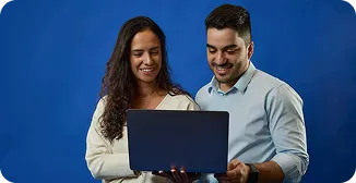 Um homem e uma mulher seguram um notebook, olham para tela enquanto sorriem.