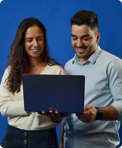 Um homem e uma mulher seguram um notebook, olham para tela enquanto sorriem.