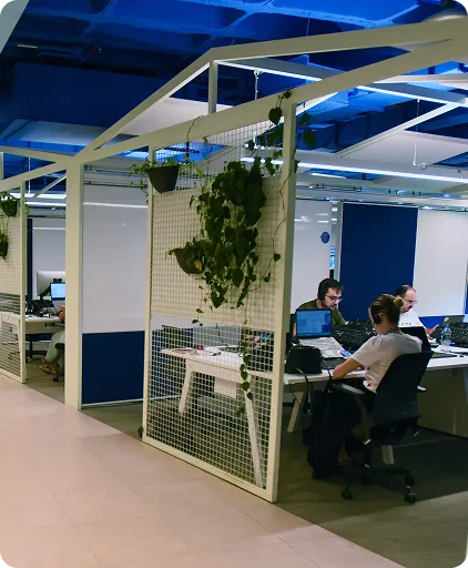 Em um ambiente corporativo, algumas pessoas estão sentadas em frente aos computadores.