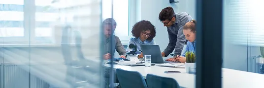 Em uma sala de reunião, pessoas conversam enquanto olham o computador.