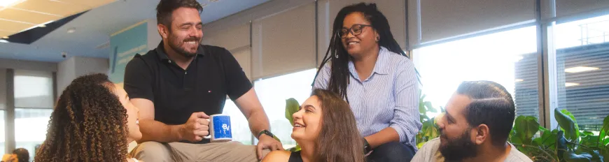 Profissionais do banco BV reunidos em local de trabalho.