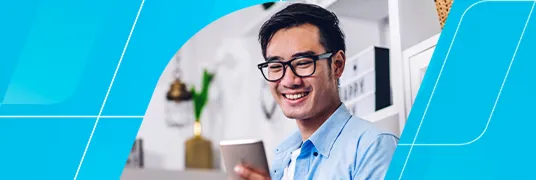 Homem branco com óculos de haste preta olhando sorridente para a tela do celular.