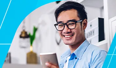 Homem branco com óculos de haste preta olhando sorridente para a tela do celular.