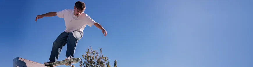 Um homem de camiseta branca, prestes a descer uma rampa de skate.