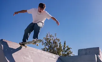 Um homem de camiseta branca, prestes a descer uma rampa de skate.