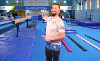 Medalhista Olímpico Diego Hypólito em um centro de treinamento de ginástica artística, apontando para trás.