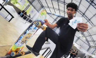 Um jovem segurando um skate em uma mão, e na outra, flyers com a logo do Instituto Sandro Dias.