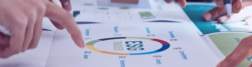 Mãos apontando para um gráfico ESG sobre mesa, discutindo dados e estratégias em ambiente de trabalho.