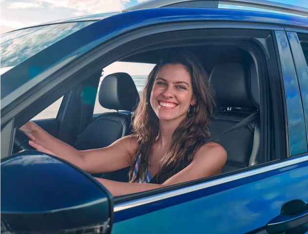 Mulher sorridente dentro de um carro com as mãos ao volante.