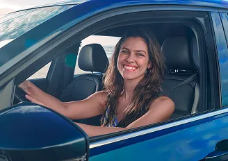 Mulher sorridente dentro de um carro com as mãos ao volante.