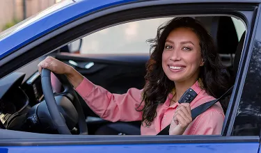 Mulher alegre e sorridente no volante de um carro, enquanto segura uma chave.