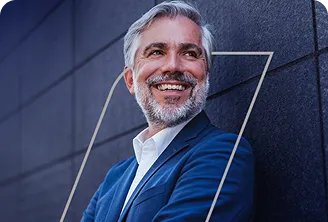 Na imagem, temos um homem executivo em pé, encostado em uma parede.