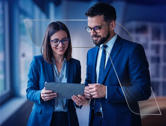 Em um ambiente corporativo, uma mulher e um homem estão com roupa social olhando para um tablet e sorrindo.