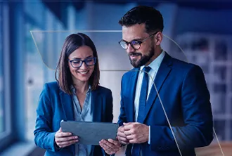 Em um ambiente corporativo, uma mulher e um homem estão com roupa social olhando para um tablet e sorrindo.