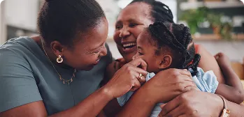 Duas mulheres negras abraçando e sorrindo uma criança.