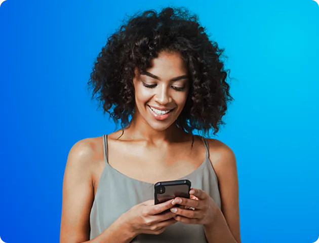 Uma mulher negra de cabelos cacheados na altura no queixo, segura o celular com as duas mãos e sorri.