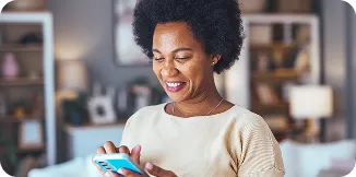 Uma mulher negra de cabelos cacheados curtos, segura o celular com as duas mãos e sorri.