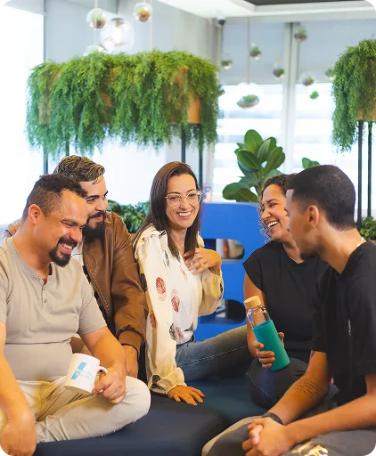Cinco pessoas conversando e sorrindo em um ambiente corporativo moderno, com plantas ao fundo.