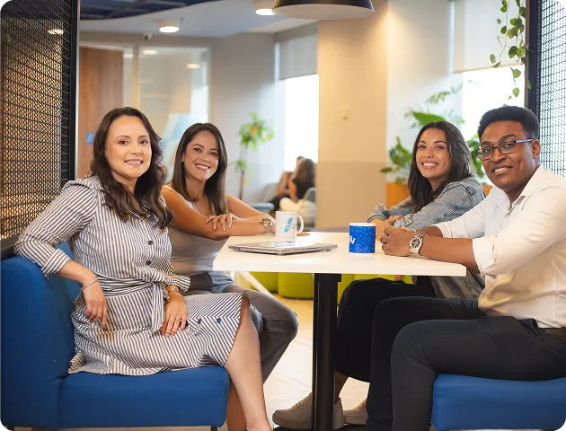 Um homem e três mulheres sorridentes, sentados ao redor de uma mesa em um ambiente corporativo. 