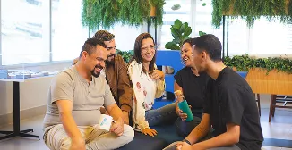 Cinco pessoas conversando e sorrindo em um ambiente corporativo moderno, com plantas ao fundo.