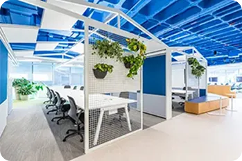 O escritório tem mesas brancas com cadeiras pretas e divisórias azuis.